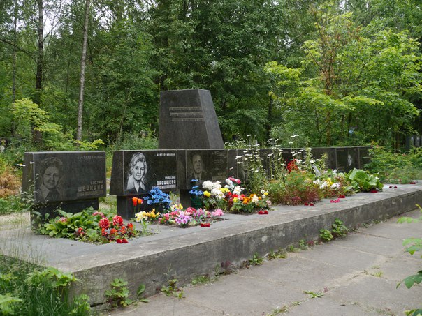 Меморіал з чорними гранітними плитами та фотографіями, оточений квітами і зеленими рослинами.